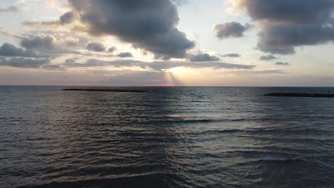 Aerial-low-fly-toward-the-sunset-over-the-clam-dark-sea,-lines-of-clouds,-drone-shot