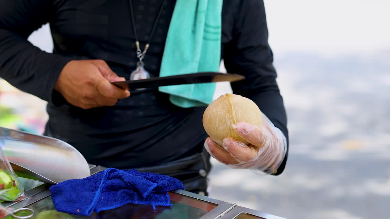 Vendor skillfully slices coconut with machete at outdoor market, natural daylight, close-up perspective