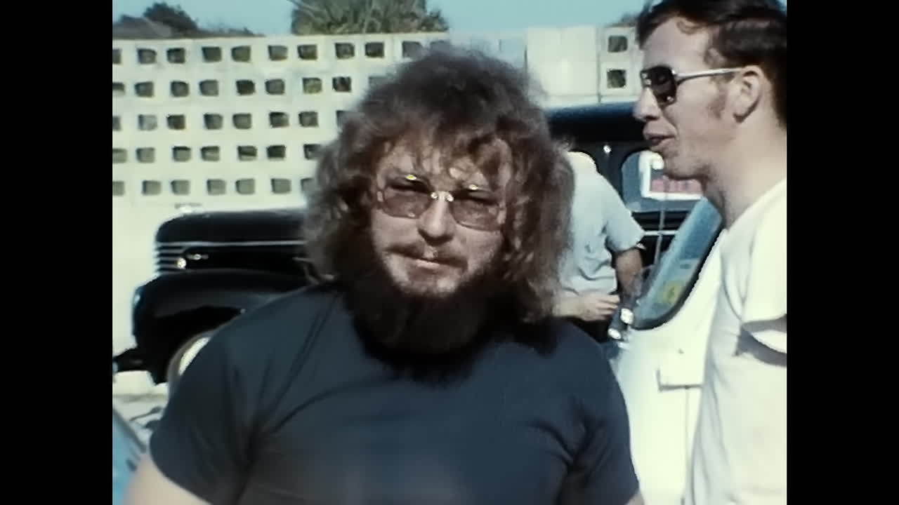 Man Driving Vintage Car Down Street at 1970s Old Car Show in USA. CIRCA USA - 1970s: A man in the drivers seat of a vintage car navigates down a street lined with onlookers at an old car show held in the 1970s in the United States.