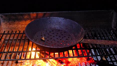 rusty perforated chestnut cooking, roasting pan on opem fire, close up, dark barckground