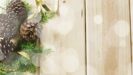christmas decorations with pinecones and ribbons over bokeh lights animation on wooden background