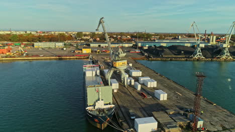 Aerial-drone-rotating-shot-over-shipping-containers-being-been-loaded-onto-a-container-ship-over-a-harbour-at-sunrise