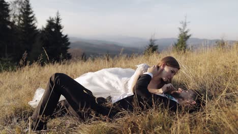 Newlyweds.-Caucasian-groom-with-bride-lie-on-the-grass-on-mountain-slope