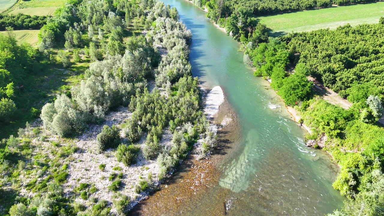 Korkealta kuvattu dronekuva vangitsee turkoosin joen veden virtaavan tiheiden vihreiden puiden ohi Italiassa.