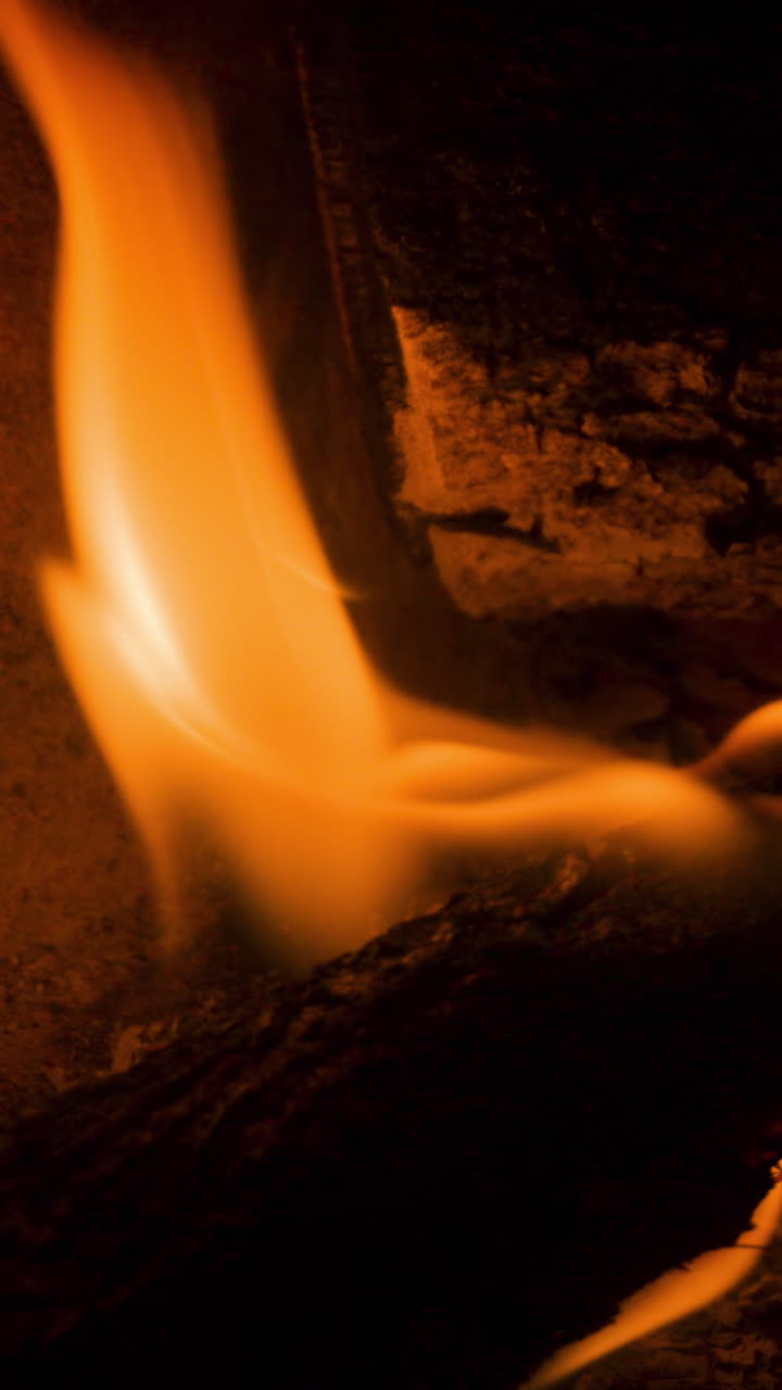 Un primer plano de llamas en un fuego de leña ardiendo en una chimenea en vertical