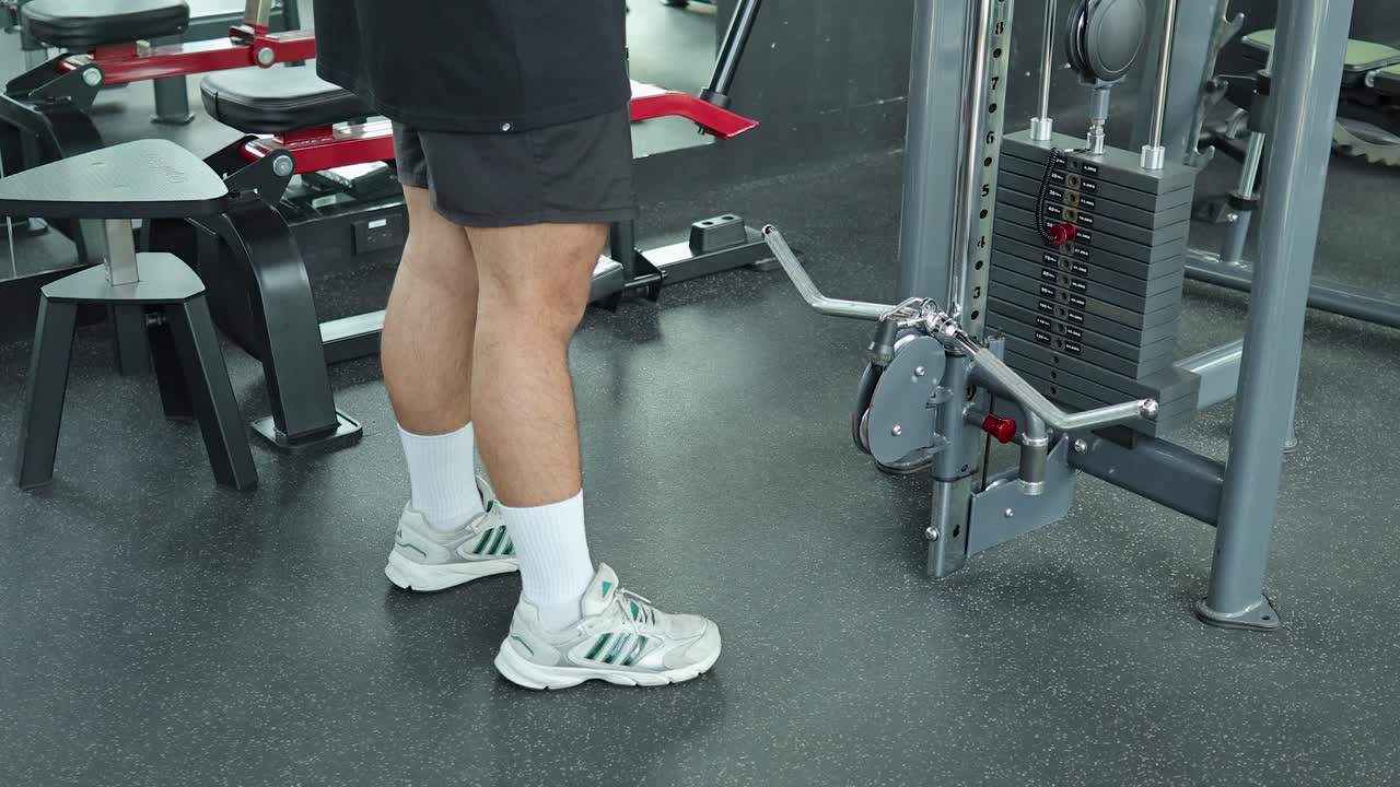 Athletic man in sleeveless shirt checks smartphone by cable machine in bright modern gym