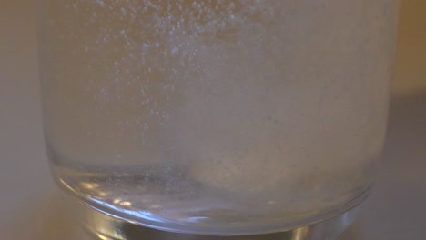 slow motion close up of white tablet dropping into clear drinking glass of water and dissolving into a fizz cloudy liquid