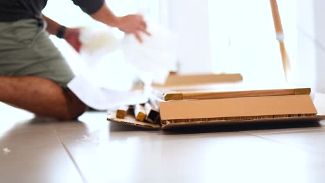 a person unpacks a cardboard box on a sunlit floor, revealing wrapped items. natural lighting creates a warm atmosphere