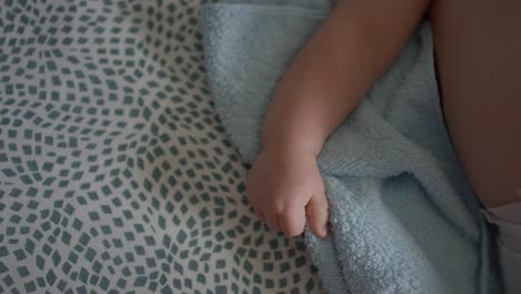 Close-up-of-a-baby's-hand-resting-on-a-patterned-blanket-and-a-soft-blue-towel,-highlighting-a-tender-and-peaceful-moment