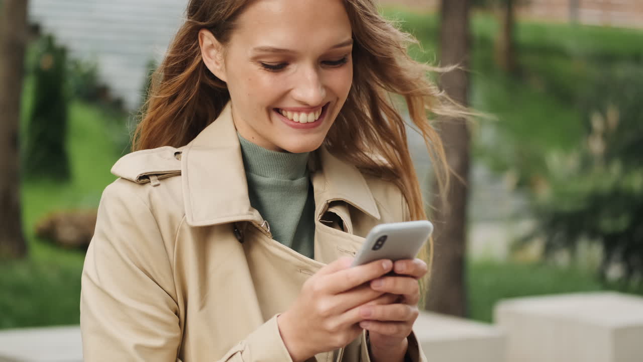 Happy Caucasian female student using smartphone outdoors.
