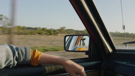 Frau-Hält-Die-Hand-Aus-Dem-Autofenster-Und-Spürt,-Wie-Der-Wind-Durch-Die-Finger-Weht,-Während-Sie-Auf-Dem-Land-Fährt-Und-Im-Sommerurlaub-Unterwegs-Ist-Und-Die-Freiheit-Auf-Der-Straße-Genießt