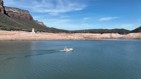 barco a motor de pescador aéreo en el embalse de sau con iglesia resurfaced detrás