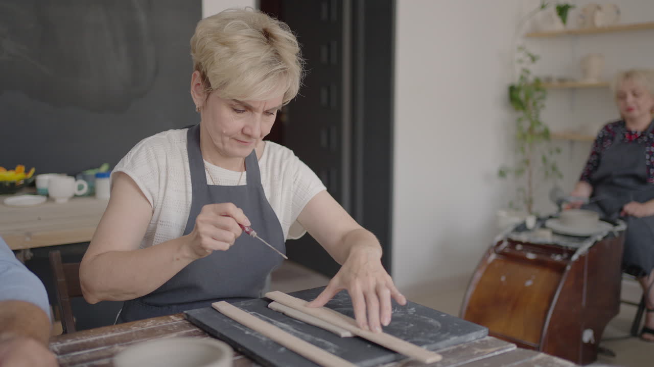Woman Potter Attaching Handle To Mug In Ceramics Studio. Female potter shaping and carving mug in pottery workshop studio