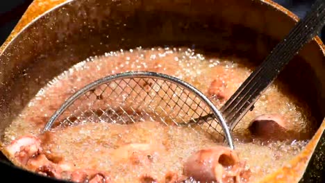 pot of bubbling hot oil deep frying seafood of calamari or baby squid in outdoor sunshine