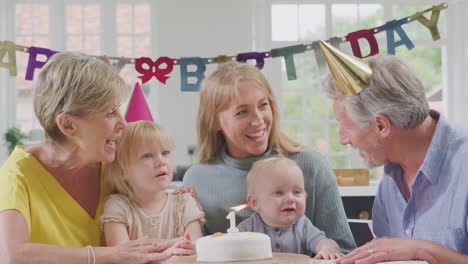 grandparents with mother singing happy birthday to grandson at first birthday party at home