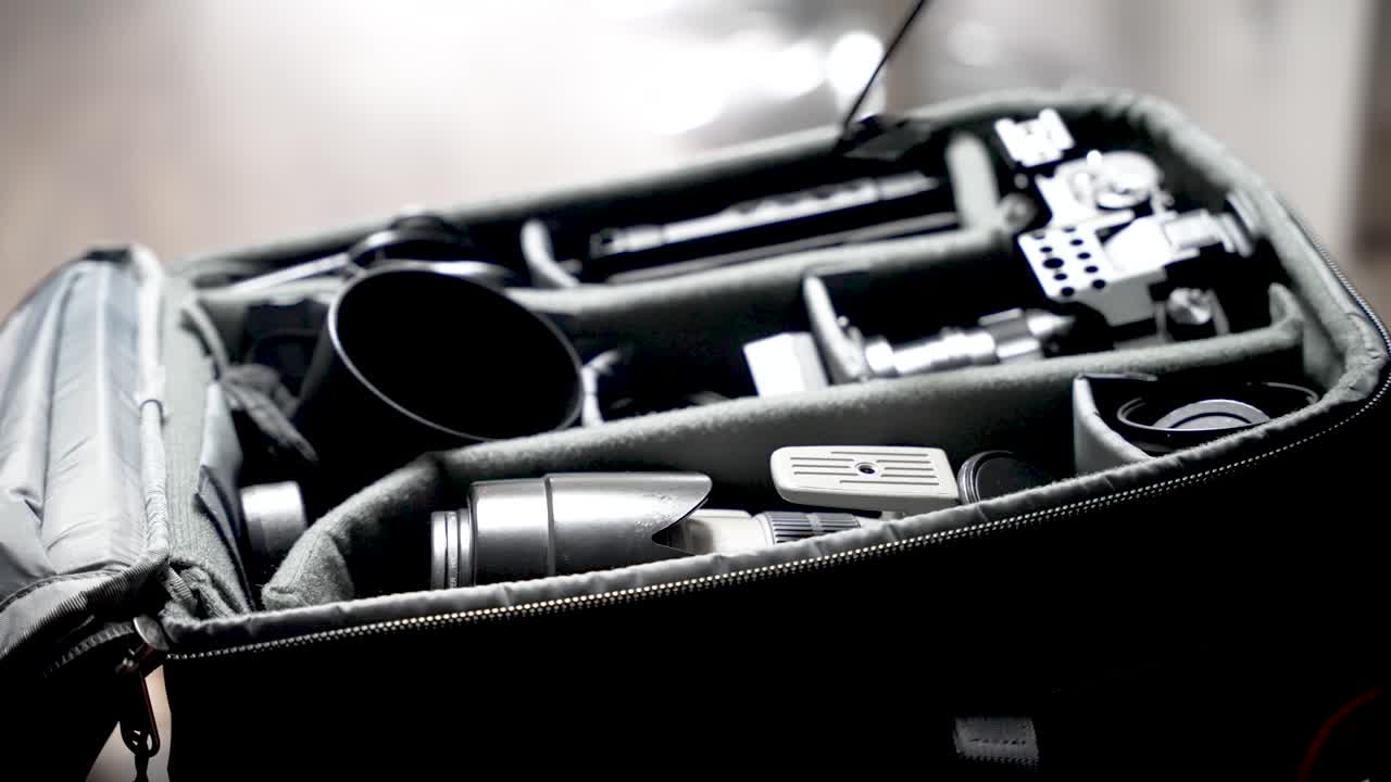 Hand placing a large lens into a partitioned bag with other camera equipment