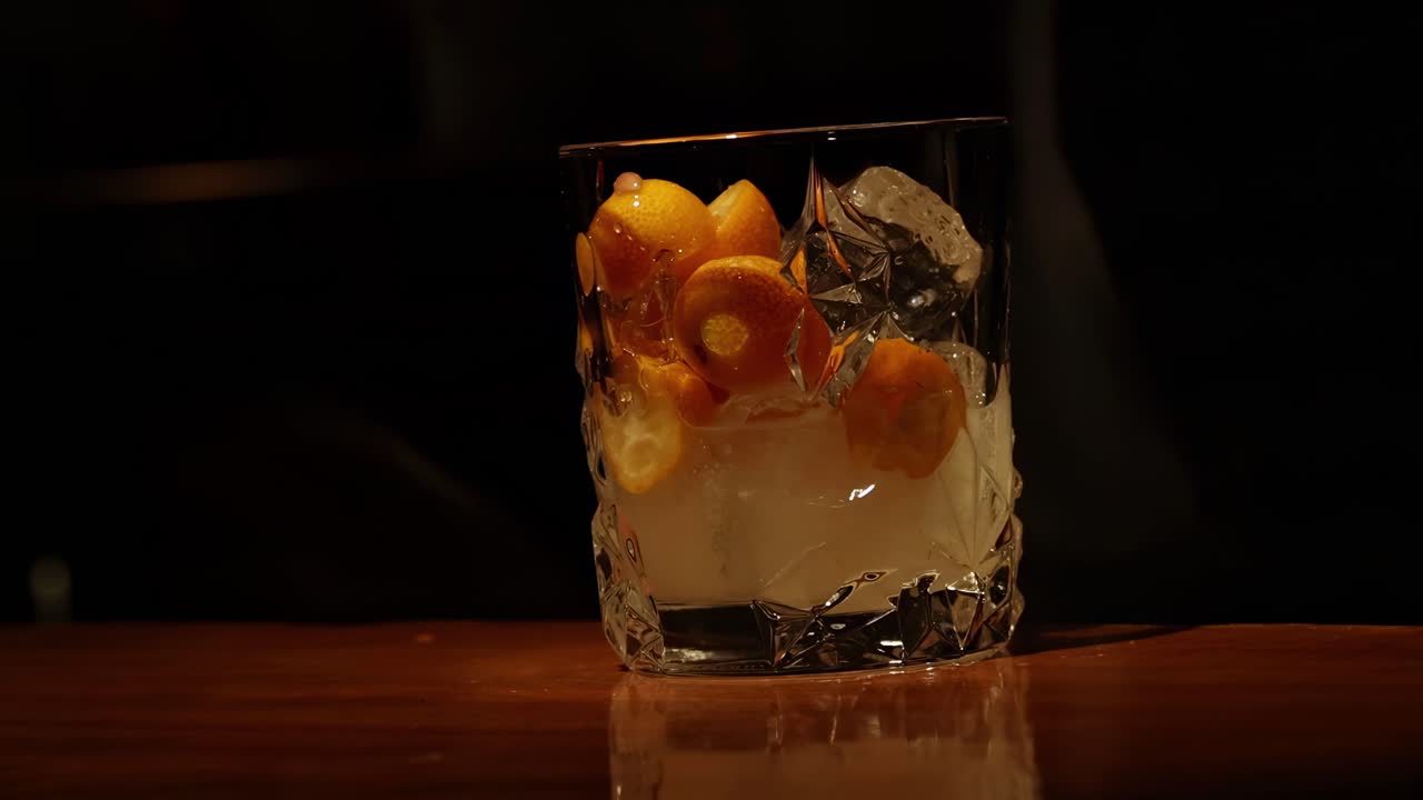 A hand carefully adjusts a citrus garnish in a glass filled with ice on a wooden counter.