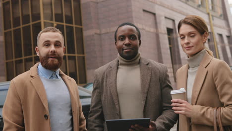 bottom view of caucasian businesswoman holding coffee, african american man watching to a tablet and caucasian man in the street in autumn