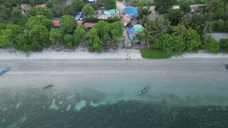 drone footage of a tropical beach with boats along the shore and lush greenery