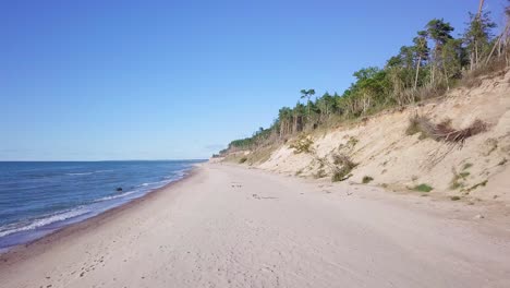 Aerial-view-of-Baltic-sea-beach-at-Jurkalne-on-a-sunny-day,-white-sand-cliff-damaged-by-waves,-coastal-erosion,-climate-changes,-wide-angle-drone-shot-moving-forward