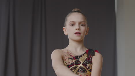 young girl in leotard practising rhythmic gymnastics with clubs in a studio while looking at camera