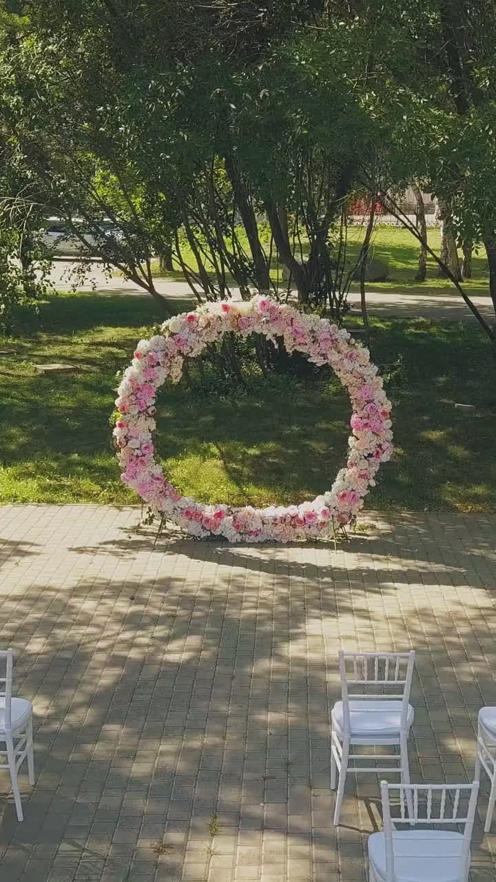 round wedding venue decorated with colorful flower garland and empty chair rows in green sunny park upper view