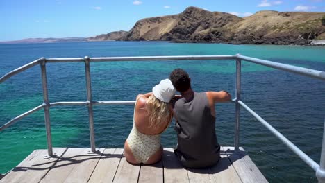 una pareja sentada en un muelle en el sur de australia mirando el hermoso océano azul brillante