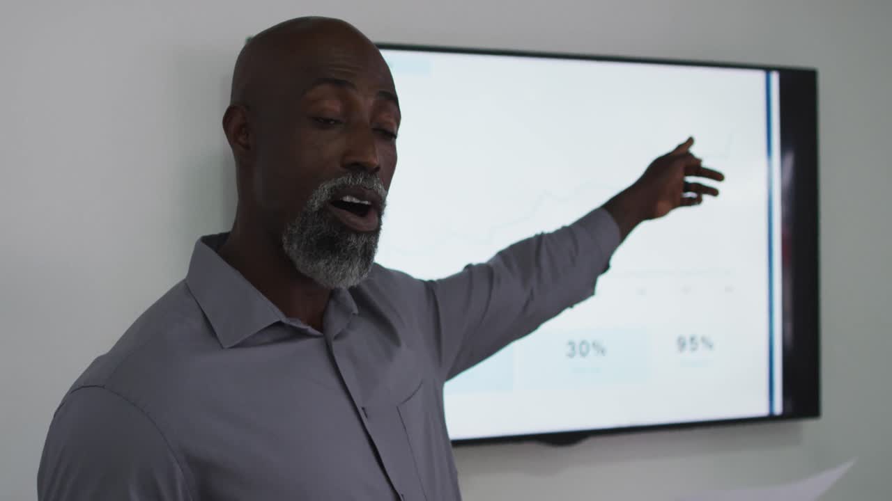 African american businessman talking and pointing at screen, giving presentation in office