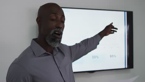 hombre de negocios afroamericano hablando y señalando a la pantalla, dando una presentación en la oficina