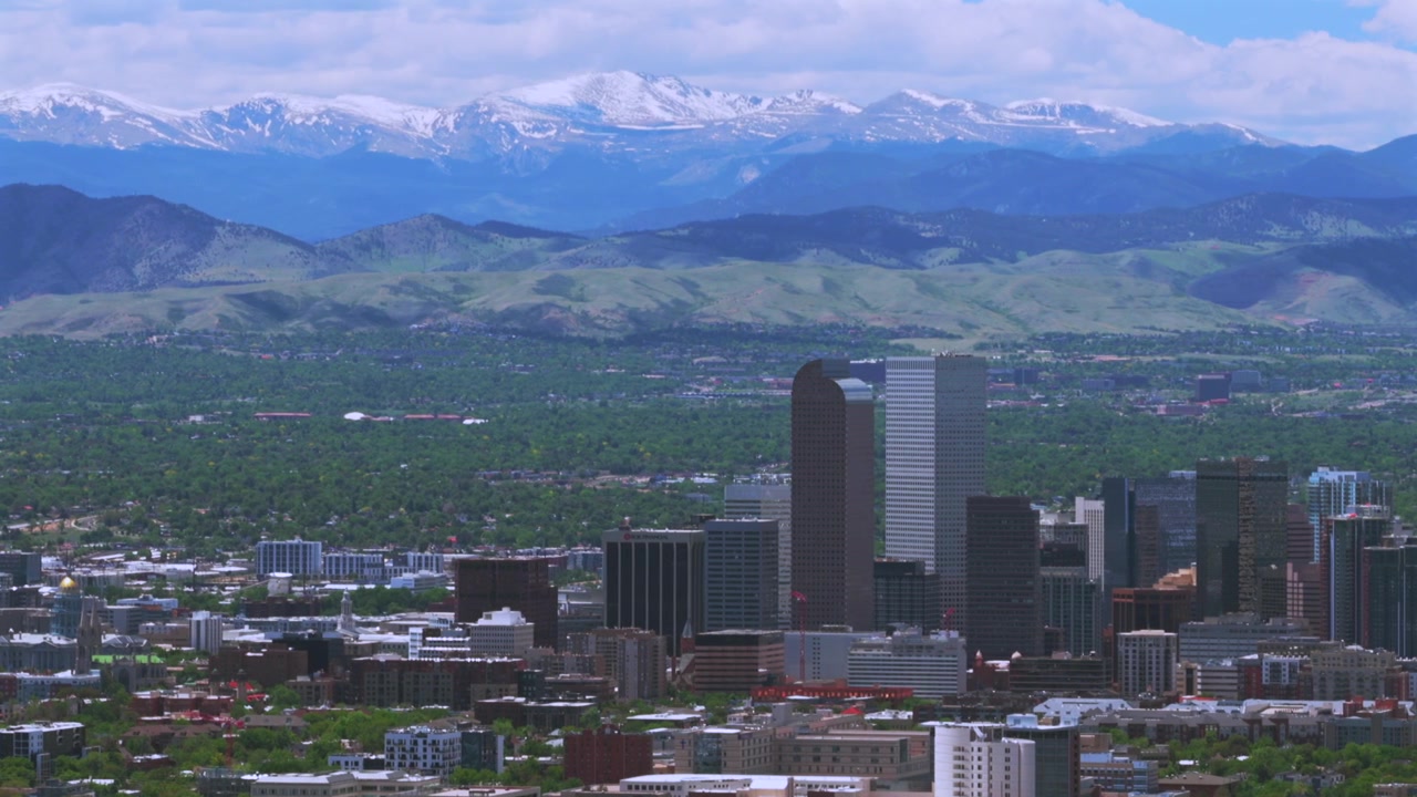 Denver, Colorado: vista aerea con drone delle Montagne Rocciose della Front Range innevate in primavera, centro di Denver, skyline della città, grattacieli, paesaggio urbano, quartieri, cielo blu mattutino, nuvole, movimento circolare a sinistra.