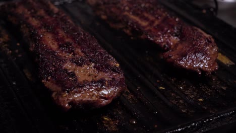 two charred beef steaks sizzling on cast iron griddle grill, closeup