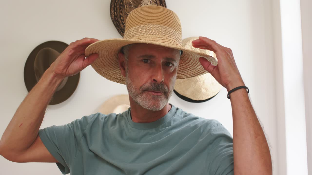 Un uomo maturo, guardando in basso, solleva un cappello di paglia a tesa larga, posizionandolo e aggiustandolo mentre è a casa.