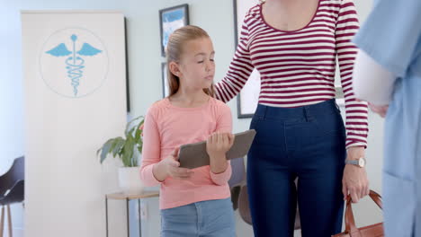 Caucasian-girl-patient-using-tablet-with-mother-and-female-in-hospital,-copy-space,-slow-motion