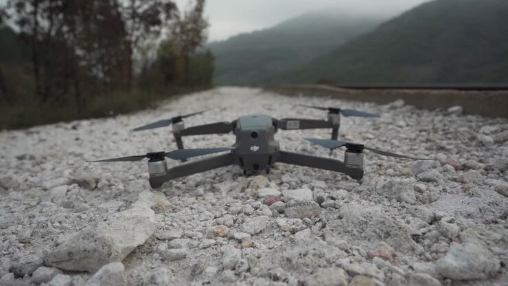 Si vede un drone DJI decollare da ghiaia bianca vicino a una ferrovia, mostrando montagne e foreste e i binari che si perdono nel paesaggio.