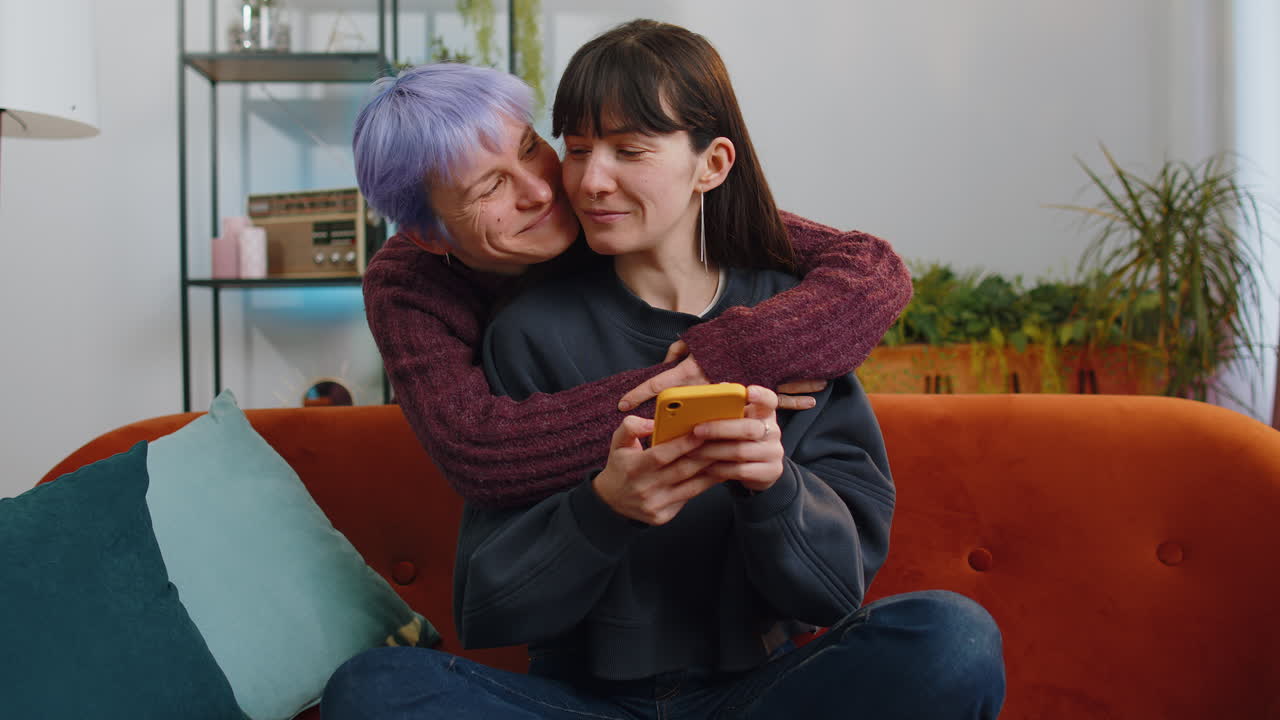 Two young lesbian women family married couple working on smartphone shopping at home living room