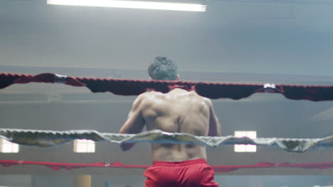 young male boxer leaning on ring rope, then doing shadow fight