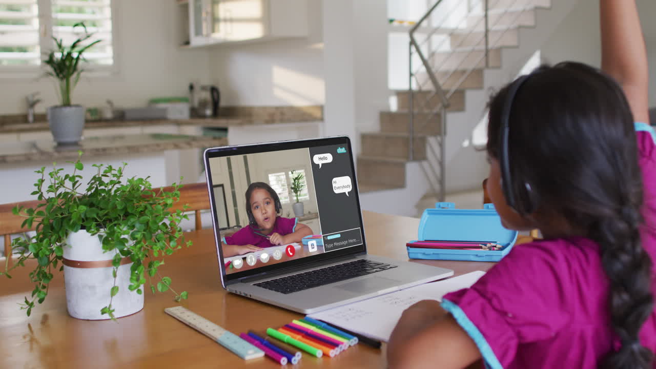Schoolgirl using laptop for online lesson at home, with her school friend and web chat on screen