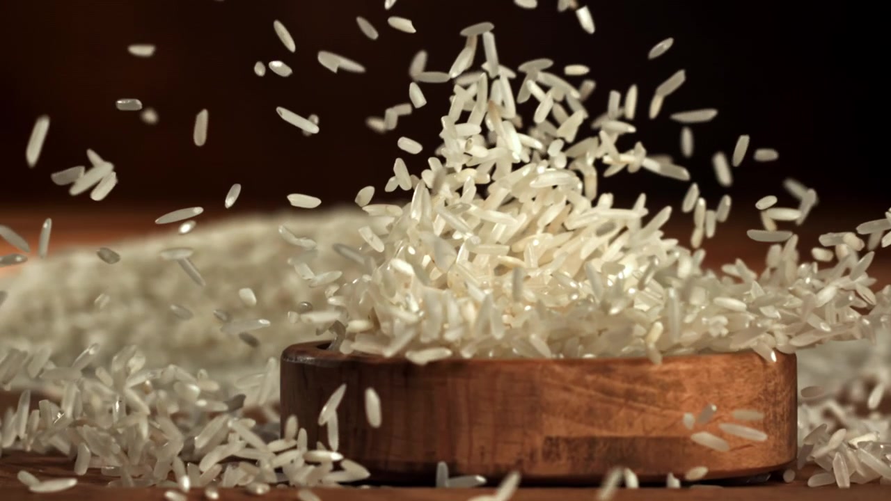 Witte rijstkorrels vallen in een houten kom in slow motion