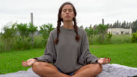 dark-haired girl sits meditating in lotus pose outdoors, close frontal