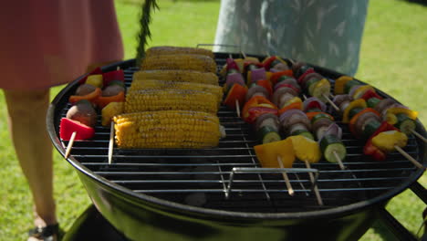 grilling colorful vegetable skewers and corn on barbecue in sunny backyard
