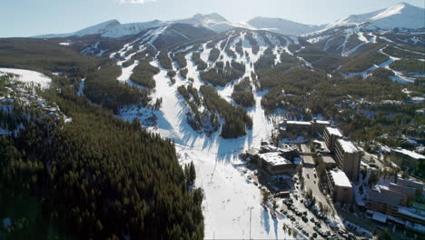 an aerial view of the popular breckenridge ski resort in colorado, with snow covered mountain peaks and high altitude trails full of winter skiers and snowboarders on a sunny winter day.