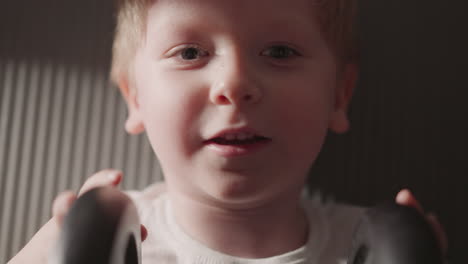 Positive-little-boy-holds-barbell-in-hands-looking-in-camera