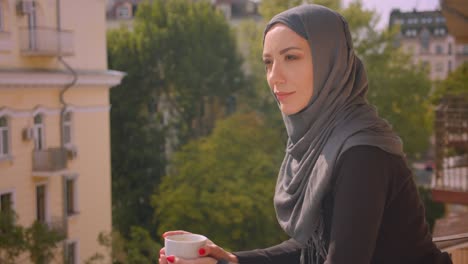 closeup portrait of young attractive muslim woman in hijab looking at landscape standing on balcony of the house