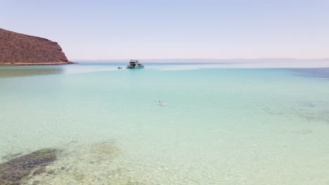 Aerial:-holidaymaker-swimming-in-turquoise-sea-near-luxury-yacht,-tropical-bay-of-Balandra-Beach