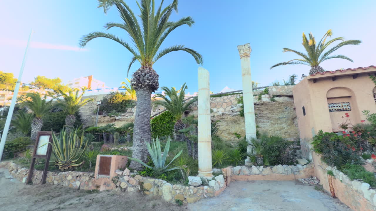 Ruins-inspired columns surrounded by exotic plants and palm trees in the Mediterranean village of Roc de Sant Gaietà, Costa Dorada, during a bright sunny morning