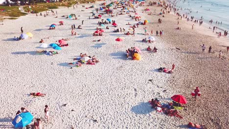 Spektakuläre-Luftkippe-über-Einem-überfüllten-Und-Geschäftigen-Ferienstrand-In-Camps-Bay-Kapstadt-Südafrika-Mit-Zwölf-Aposteln-Berghintergrund