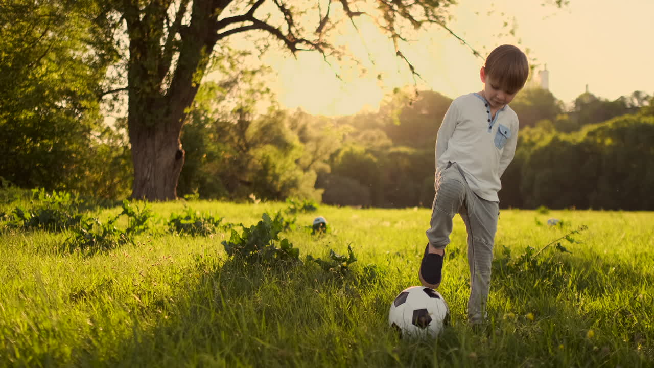 un niño de pie con una pelota de fútbol en el verano al atardecer mirando a la cámara.