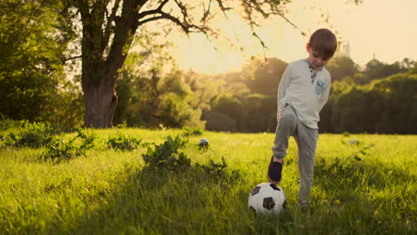 Junge-Steht-Im-Sommer-Mit-Einem-Fußball-Bei-Sonnenuntergang-Und-Schaut-In-Die-Kamera.