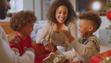 family exchanging and opening gifts around christmas tree at home