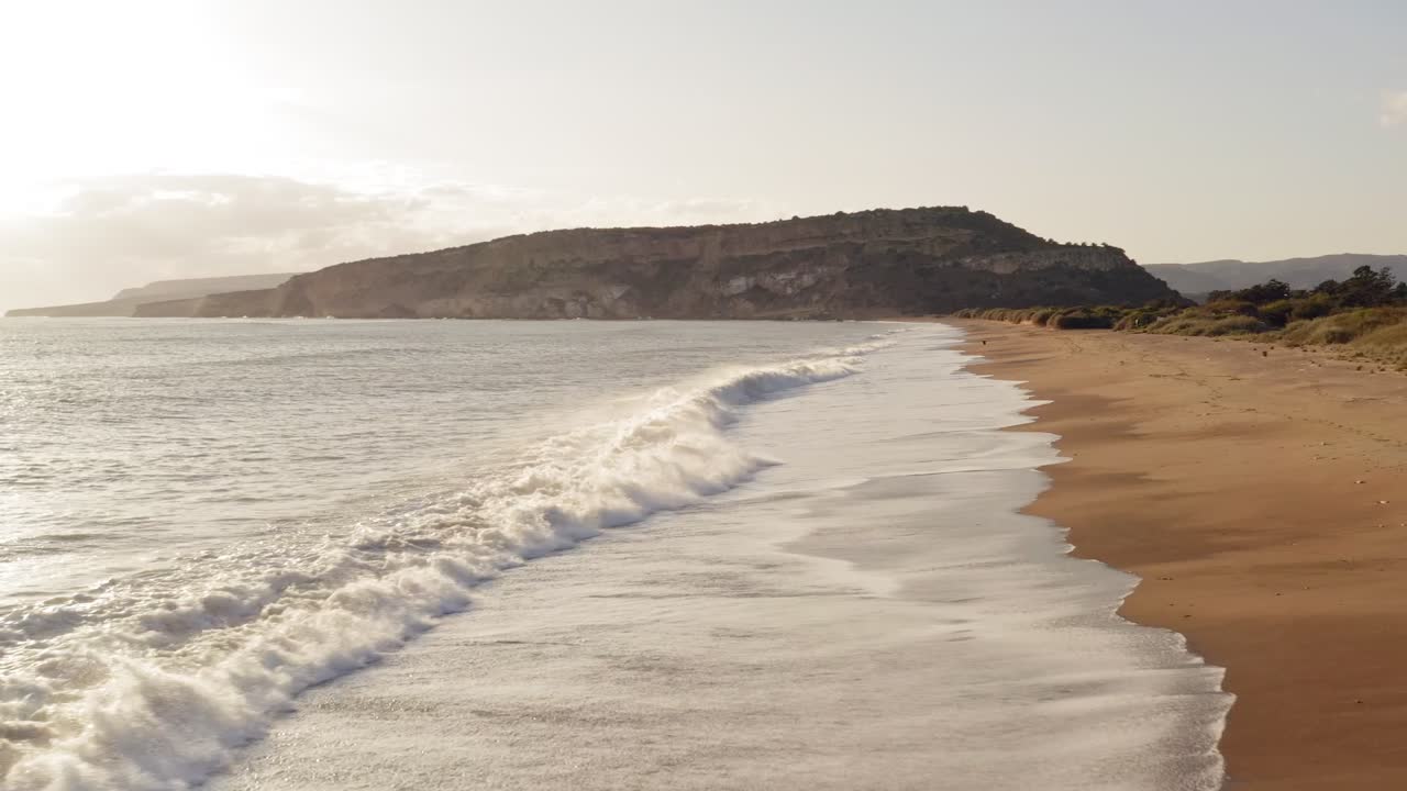 Luftfoto af en malerisk gylden sandstrand, hvor bølger slår ind mod kysten.